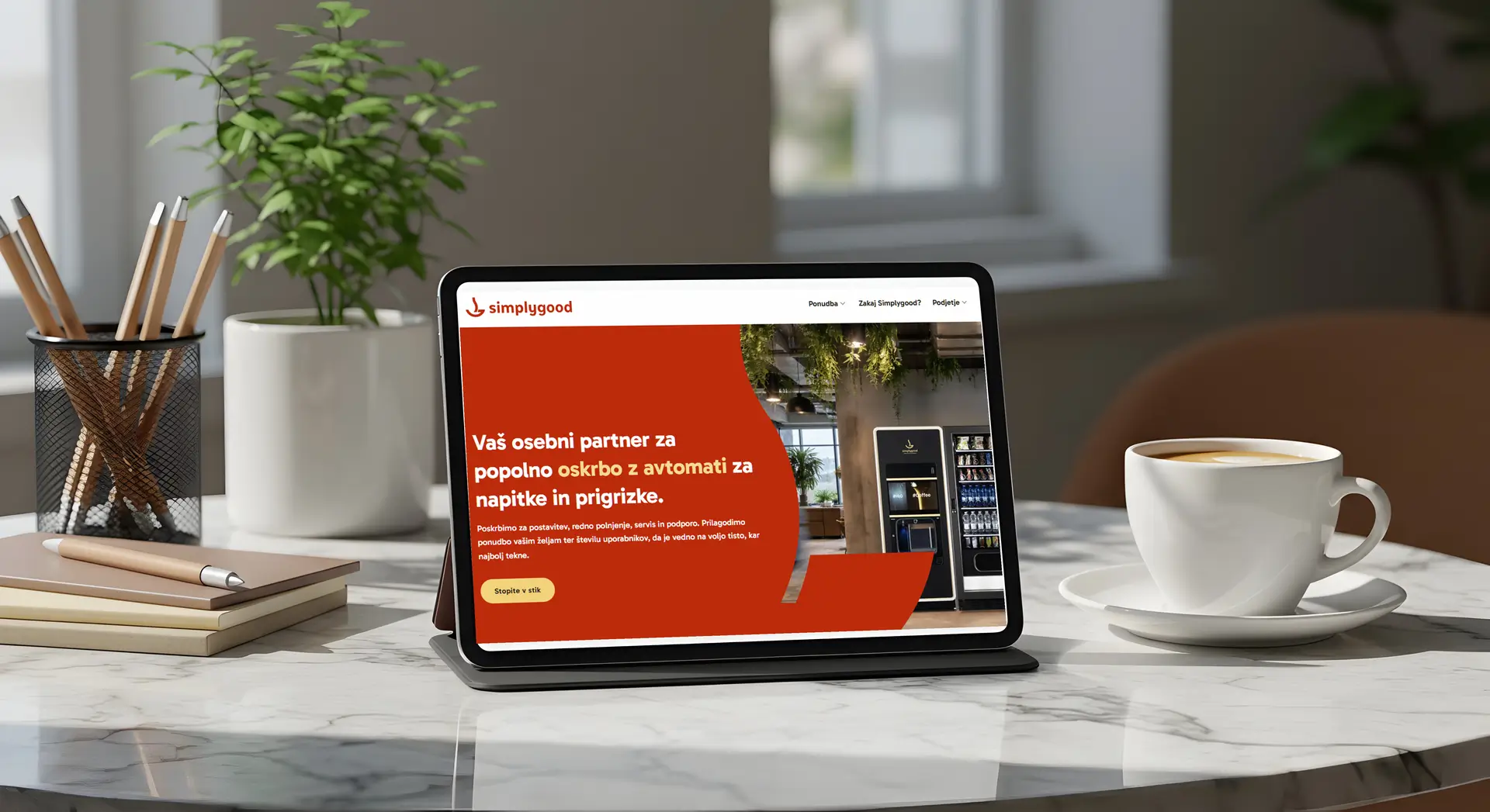 Tablica, ki prikazuje spletno stran Simplygood in skodelica kave na pisarniški mizi