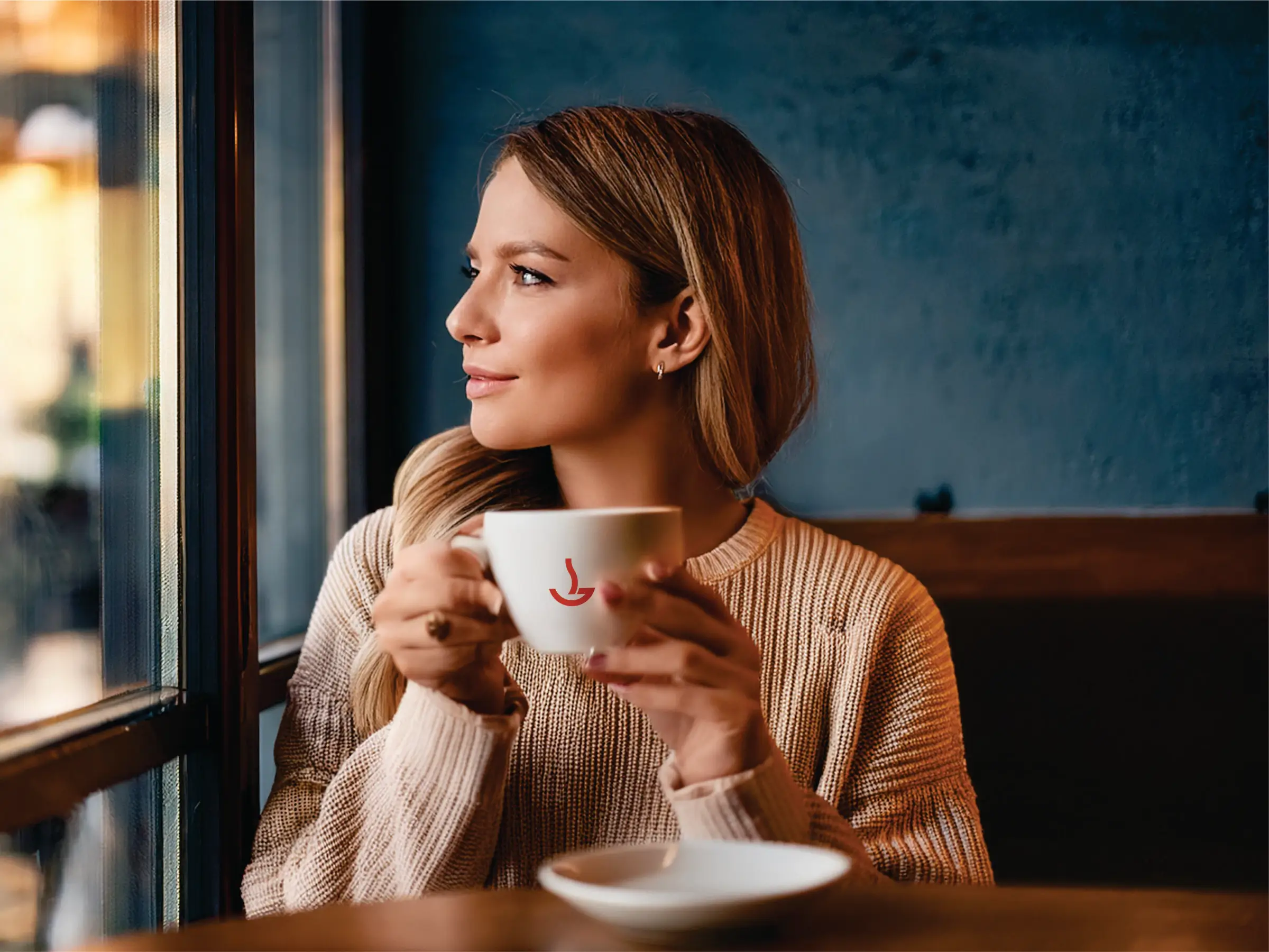 Ženska uživa kavo ob oknu v prijetnem ambientu